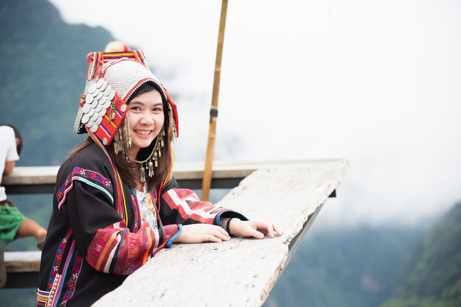 Una mujer joven sonríe vistiendo un traje y un tocado tradicional ornamentado de una etnia China